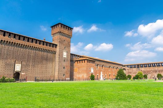 Tower of Porta Giovia and brick walls of old medieval Sforza Castle Castello Sforzesco with green lawn of courtyard and blue sky white clouds background, Milan, Lombardy, Italy