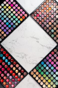 Flat lay of cosmetic eyeshadow palettes on white marble background. Rhombus frame for your copy