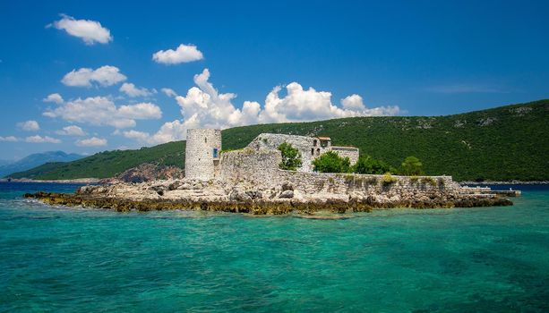 Monastery and church Vavedenja Presvete Bogorodice on island Mala Gospa near Zanjic on Lustica peninsula, Boka Kotor bay with blue turquoise paradise water, blue sky, white clouds, Montenegro