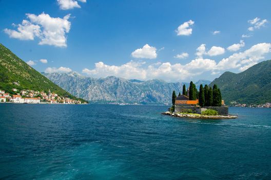 Saint George Benedictian monastery and church on St. George island Ostrvo Sveti Dorde in Boka Kotor bay near Perast town in front of mountains range and blue sky with white clouds, Montenegro