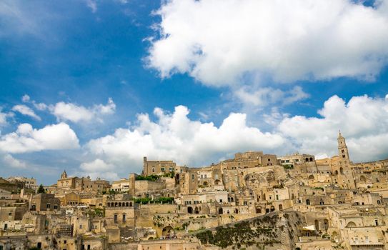 Sassi di Matera panoramic view of historical centre Sasso Caveoso of old ancient town with rock cave houses in front of blue sky and white clouds, UNESCO World Heritage, Basilicata, Southern Italy