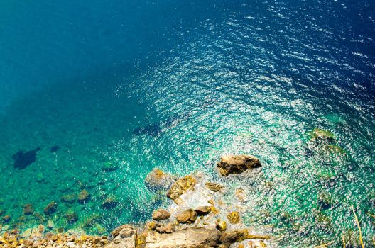 Top view from castle Castello Ruffo of seaside stone rock shore coast of turquoise green blue water with sunlight reflection off water surface of Tyrrhenian sea, Scilla, Calabria, Southern Italy