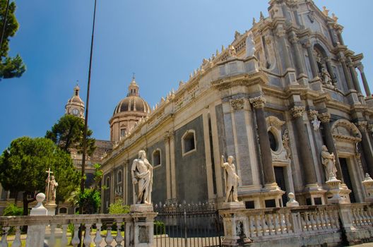 Cathedral of Santa Agatha with green trees nearby on Piazza del Duomo square in beautiful summer day in Catania city, Sicily, Italy