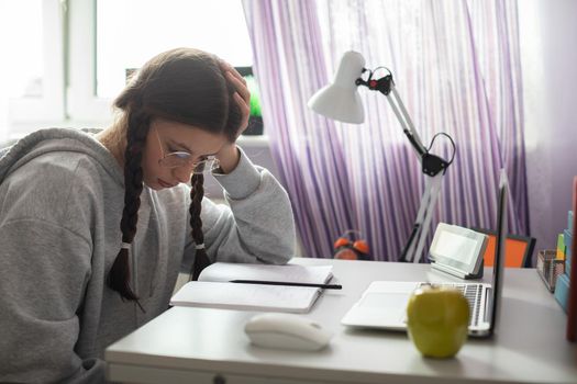 A student is thinking and thinking about how to solve a complicated assignment she received from school to do at home. A diligent student. Remote learning at home.