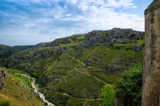 View of ravine canyon with rocks and houses in caves di Murgia Timone near old ancient town Matera (Sassi) with blue sky ant white clouds, UNESCO World Heritage, Basilicata, Southern Italy