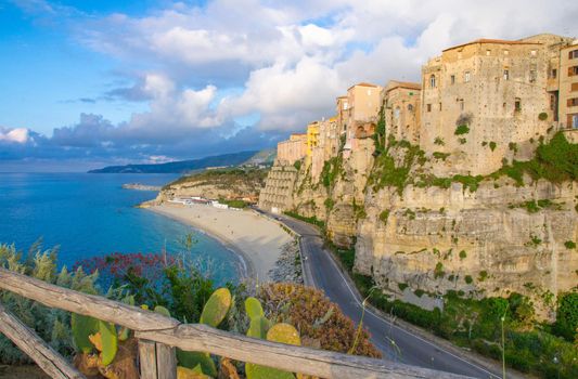 Tropea town and Tyrrhenian Sea beach, colorful buildings on top of high big rocks, view from Sanctuary church of Santa Maria dell Isola with fence foreground, Vibo Valentia, Calabria, Southern Italy