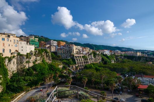 Tropea town, green trees in park, colorful buildings on top of high big steep rock cliff, view from Sanctuary church of Santa Maria dell Isola, Vibo Valentia, Calabria, Southern Italy