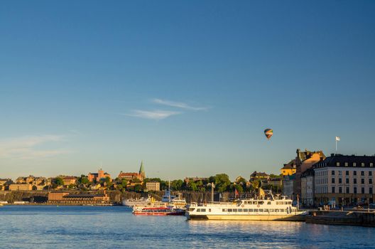 View of Sodermalm island coast near Lake Malaren water and boats ships near Gamla Stan embankment and hot air balloon with blue clear sky copy space, Stockholm, Sweden