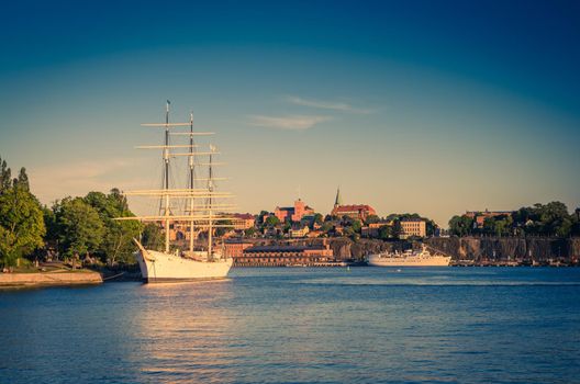 White ship yacht boat hostel af Chapman with mast moored on Lake Malaren water near Skeppsholmen island with green trees, Sodermalm island background in front of blue sky, Stockholm, Sweden