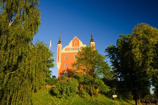 Admiralty House building with spires on Skeppsholmen island near Skeppsholm bridge with green trees around and blue clear sky background, Stockholm, Sweden