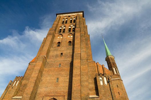 Brick building tower with spires of Basilica Assumption Blessed Virgin Mary St Marys Church Cathedral on Piwna street with blue sky white clouds background, Gdansk, Poland
