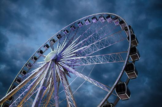 Big luminous ferris wheel in front of dark blue dramatic sky background in the evening at night, Gdansk, Pomerania, Poland