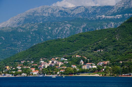 View of Boka Kotor bay water, town of Herceg Novi and Mount Orjen of Dinaric Alps mountain range in front of blue sky with white clouds, Montenegro