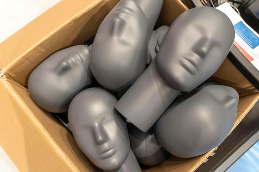 gray plastic mannequin heads are in a cardboard box. a bunch of mannequin heads in the store.