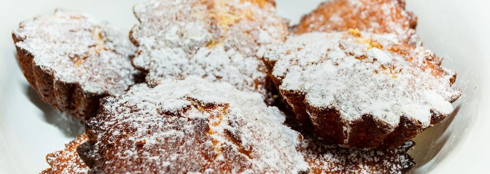 Freshly baked cupcakes in a plate sprinkled with powdered sugar close-up. Side view. Culinary theme.