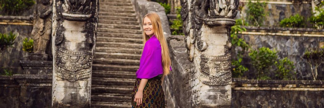 BANNER, LONG FORMAT Young woman tourist on background of Three stone ladders in beautiful Pura Lempuyang Luhur temple. Summer landscape with stairs to temple. Paduraksa portals marking entrance to middle sanctum jaba tengah of Pura Penataran Agung, Bali.