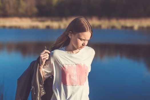 Portrait of a beautiful happy teenage girl outdoors in spring. A girl poses on lakes shore.