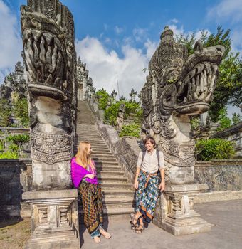 Happy couple of tourists on background of Three stone ladders in beautiful Pura Lempuyang Luhur temple. Summer landscape with stairs to temple. Paduraksa portals marking entrance to middle sanctum jaba tengah of Pura Penataran Agung, Bali.
