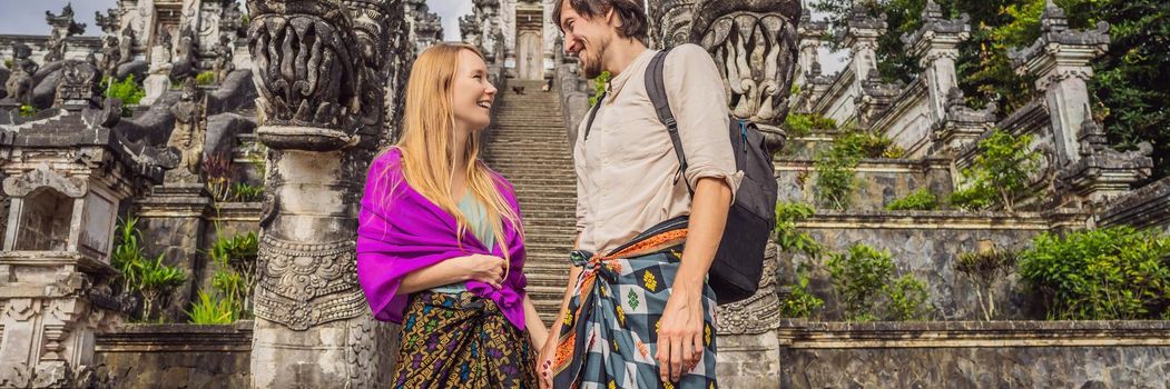 BANNER, LONG FORMAT Happy couple of tourists on background of Three stone ladders in beautiful Pura Lempuyang Luhur temple. Summer landscape with stairs to temple. Paduraksa portals marking entrance to middle sanctum jaba tengah of Pura Penataran Agung, Bali.