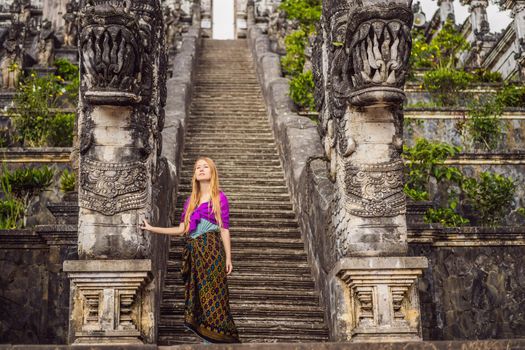 Young woman tourist on background of Three stone ladders in beautiful Pura Lempuyang Luhur temple. Summer landscape with stairs to temple. Paduraksa portals marking entrance to middle sanctum jaba tengah of Pura Penataran Agung, Bali.