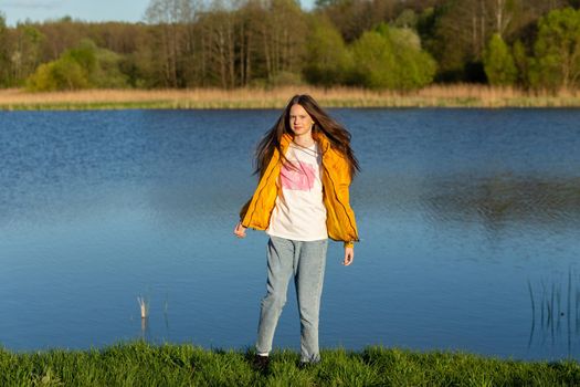 Portrait of stylish weared teenage girl outdoors in spring. A girl poses on lakes shore.