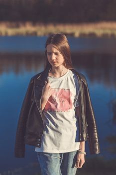 Portrait of a beautiful happy teenage girl outdoors in spring. A girl poses on lakes shore.