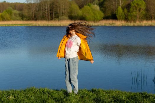 Portrait of stylish weared teenage girl outdoors in spring. A girl poses on lakes shore.