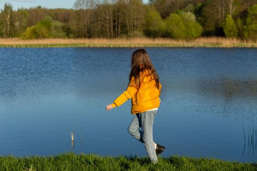 Portrait of stylish weared teenage girl outdoors in spring. A girl poses on lakes shore.