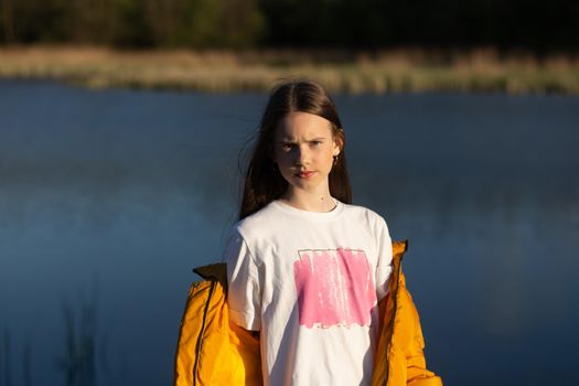 Portrait of stylish weared teenage girl outdoors in spring. A girl poses on lakes shore.