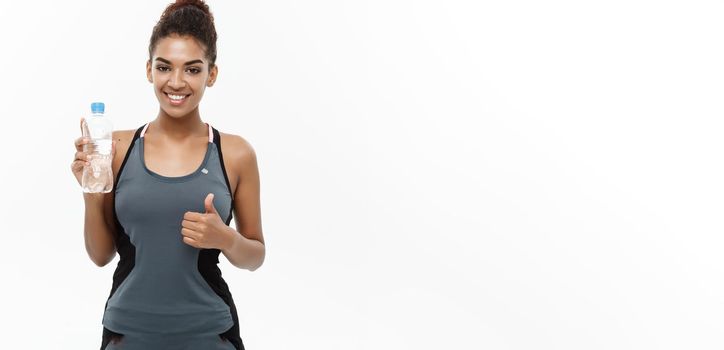 Healthy and Fitness concept - beautiful African American girl in sport clothes holding plastic water bottle after workout. Isolated on white studio background.