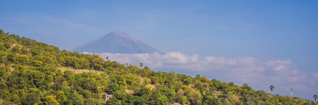 Aerial view of Amed beach in Bali, Indonesia. Traditional fishing boats called jukung on the black sand beach and Mount Agung volcano in the background, partially covered by clouds. BANNER, LONG FORMAT