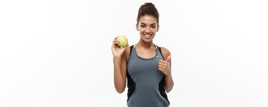 Healthy and Fitness concept - Beautiful American African lady in grey fitness clothes holding green apple. Isolated on white background