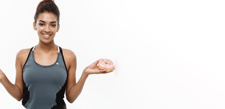 Healthy and diet concept - Beautiful sporty African American make a decision between donut and green apple. Isolated on white background