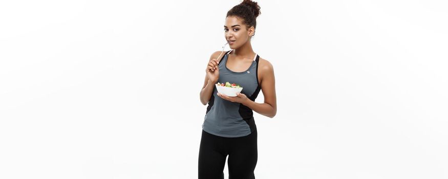 Healthy and Fitness concept - Beautiful American African lady in fitness clothes on diet eating fresh salad. Isolated on white background