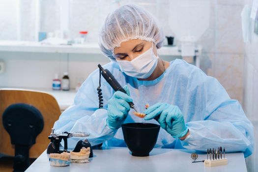 A dental technician in protective clothing is working on a prosthetic tooth in his laboratory.