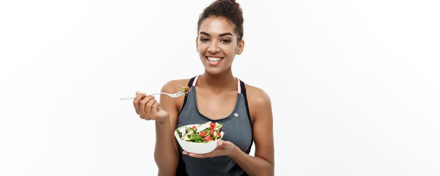 Healthy and Fitness concept - Beautiful American African lady in fitness clothes on diet eating fresh salad. Isolated on white background