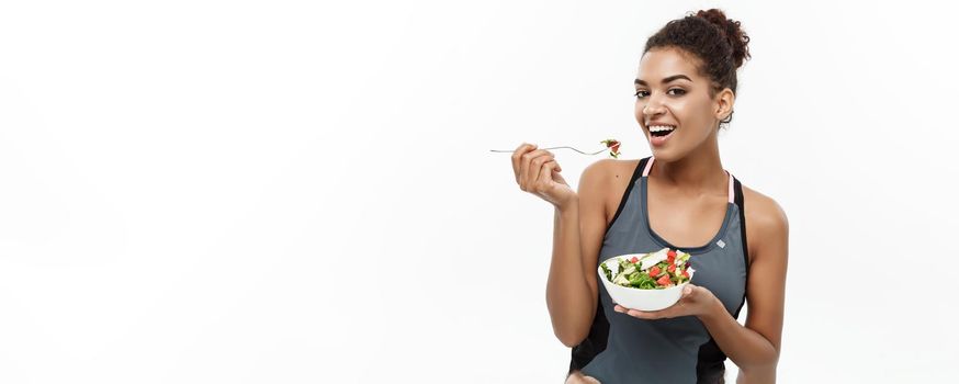 Healthy and Fitness concept - Beautiful American African lady in fitness clothes on diet eating fresh salad. Isolated on white background