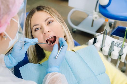 a dentist in a protective mask sits next to him and treats a patient in the dental office.