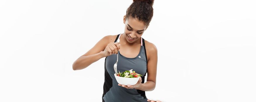 Healthy and Fitness concept - Beautiful American African lady in fitness clothes on diet eating fresh salad. Isolated on white background