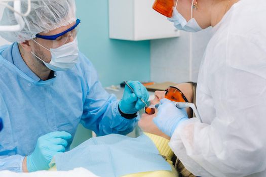 A male dentist with dental tools drills the teeth of a patient with an assistant. The concept of medicine, dentistry and healthcare.