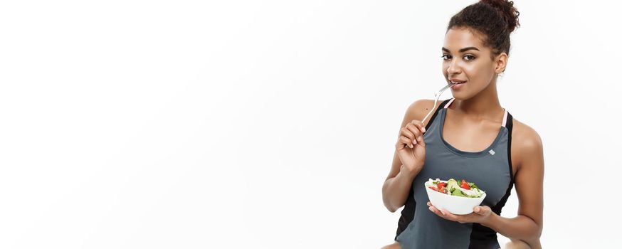 Healthy and Fitness concept - Beautiful American African lady in fitness clothes on diet eating fresh salad. Isolated on white background