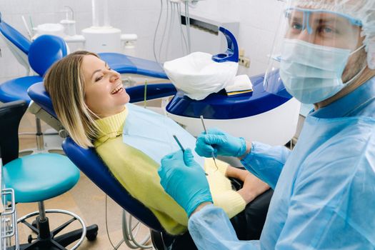 The patient smiles in the dentist's chair in a protective mask and instrument before treatment in the dental office.