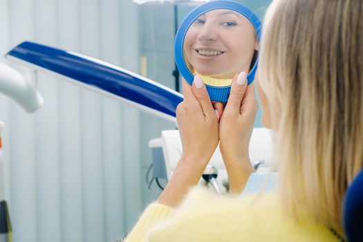 The girl smiles and looks in the mirror in dentistry.