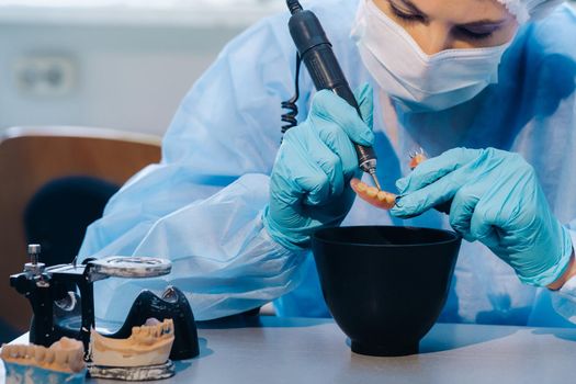 A dental technician in protective clothing is working on a prosthetic tooth in his laboratory.