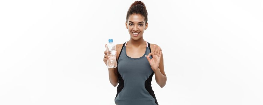 Healthy and Fitness concept - beautiful African American girl in sport clothes holding plastic water bottle after workout. Isolated on white studio background.
