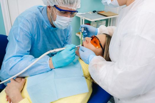 A male dentist with dental tools drills the teeth of a patient with an assistant. The concept of medicine, dentistry and healthcare.