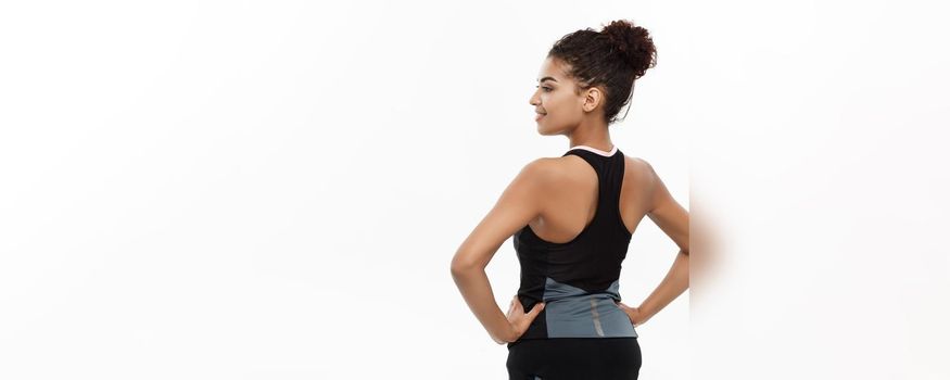 Healthy and Fitness concept - Portrait of young beautiful African American showing her back muscle with confident cheerful facial expression. Isolated on white studio background