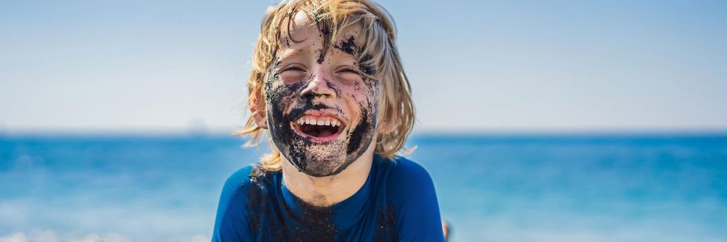 BANNER, LONG FORMAT Black Friday concept. Smiling boy with dirty Black face sitting and playing on black sand sea beach before swimming in ocean. Family active lifestyle, and water leisure on summer vacation with kids. Black Friday, sales of tours and airline tickets or goods.