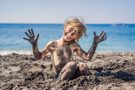 Black Friday concept. Smiling boy with dirty Black face sitting and playing on black sand sea beach before swimming in ocean. Family active lifestyle, and water leisure on summer vacation with kids. Black Friday, sales of tours and airline tickets or goods.