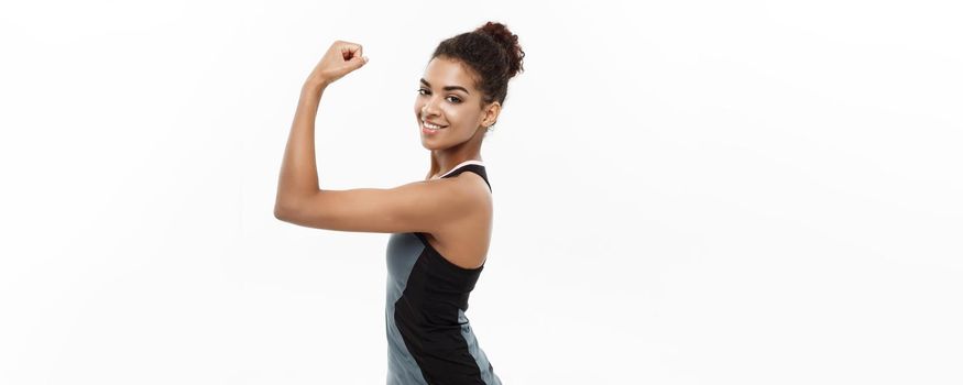 Healthy and Fitness concept - Portrait of young beautiful African American showing her strong muscle with confident cheerful facial expression. Isolated on white studio background